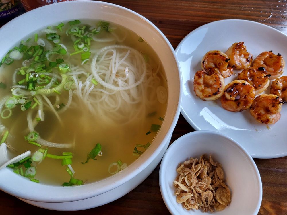 bowl of pho with scallions, hot bone broth, and shrimp on the side