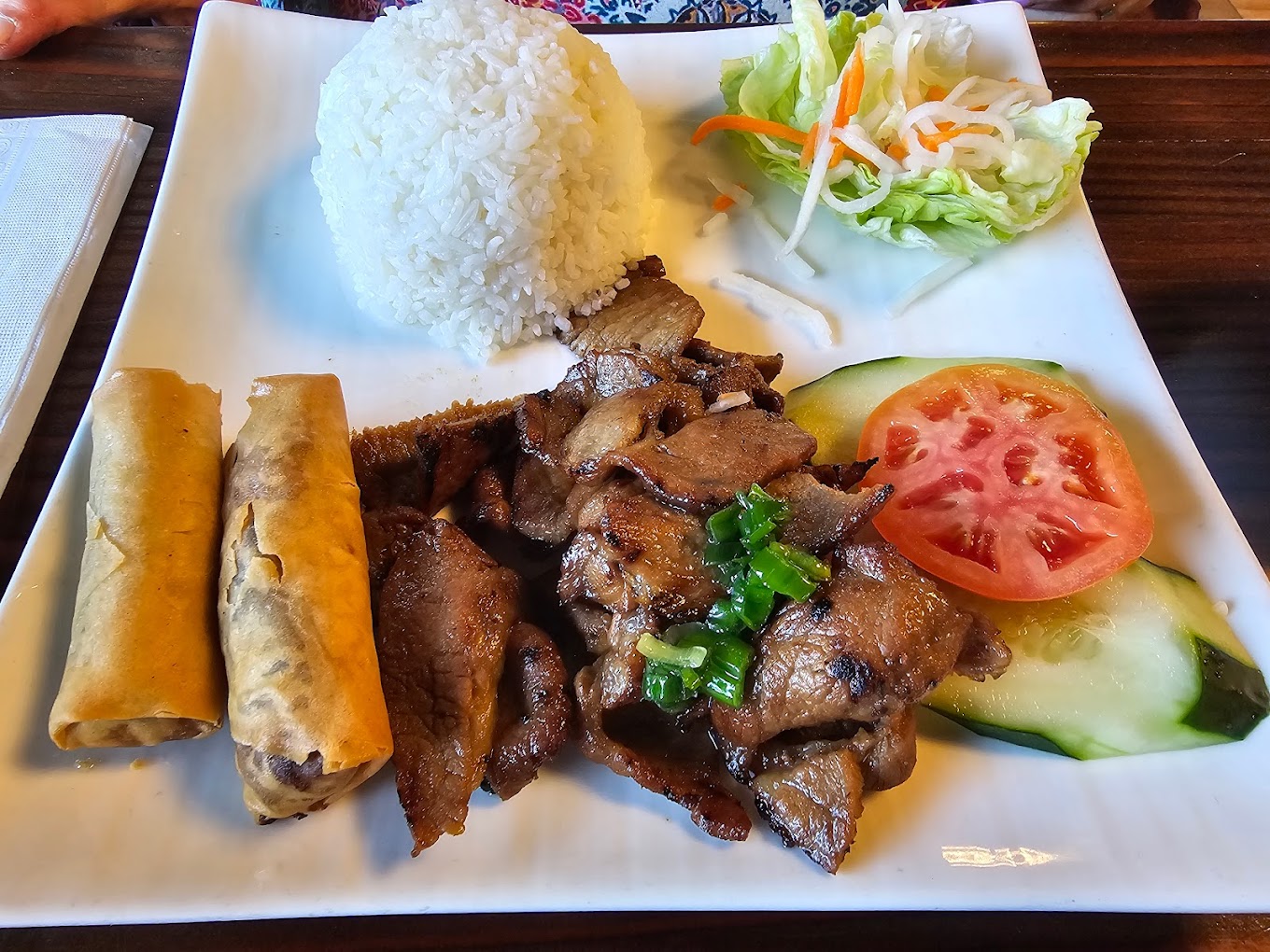 grilled pork or beef with rice, fresh vegetables, and spring rolls